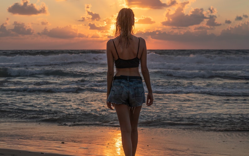 Eine sportliche Frau steht beim Sonnenuntergang am Strand